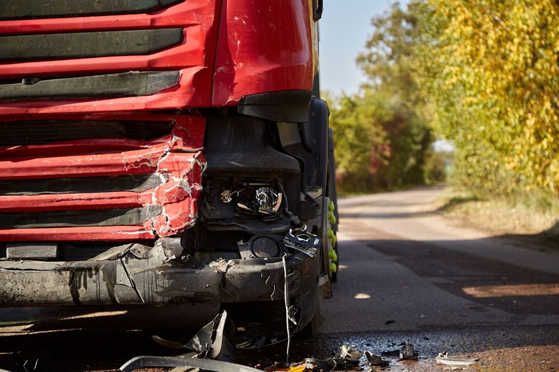 A front end of a red truck with a damaged bumper

Description automatically generated